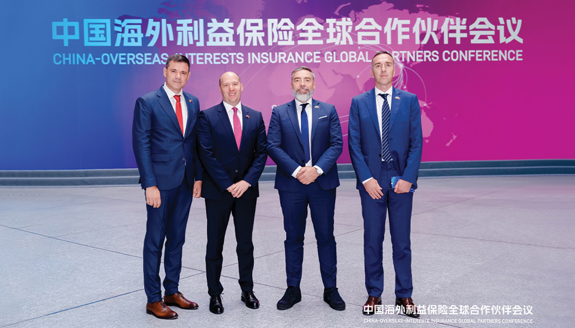 Four men standing in a big room in front of a banner displaying the name of the conference in English and Chinese.